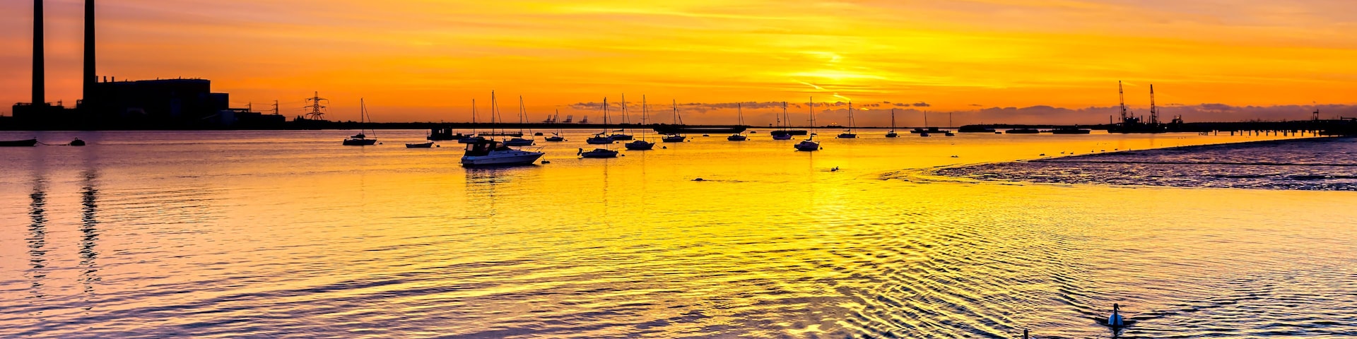 A sunset over a calm body of water with boats and a distant industrial structure.