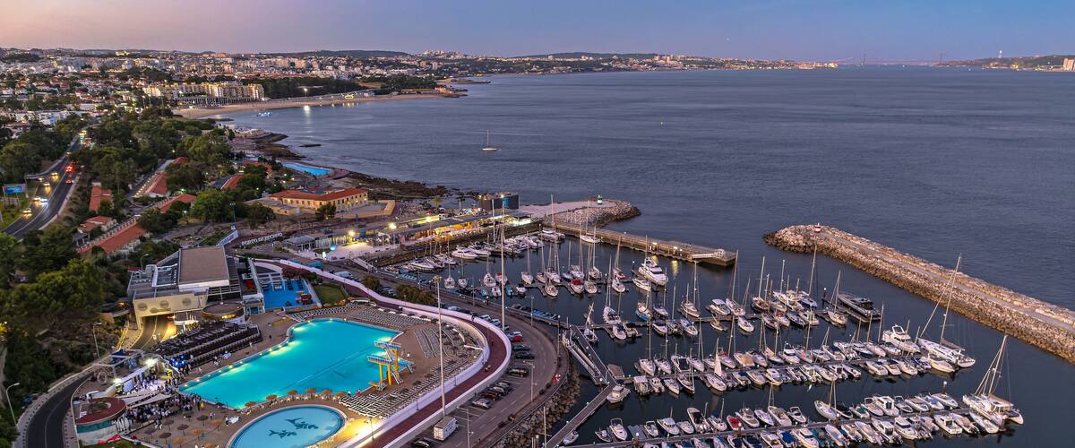 A marina with numerous boats docked, a swimming pool, and a cityscape in the background.