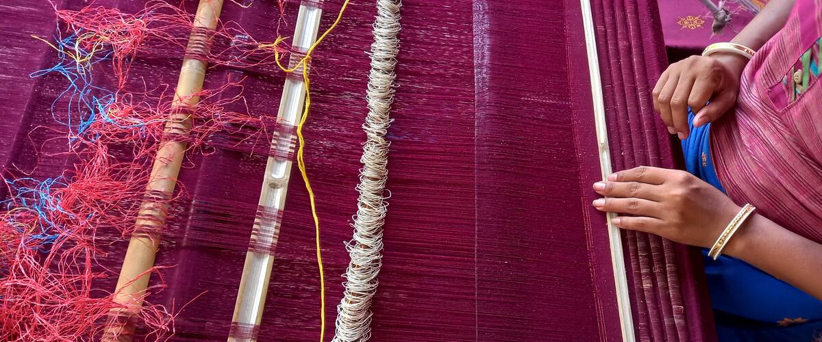 A loom with colorful threads and a person weaving.
