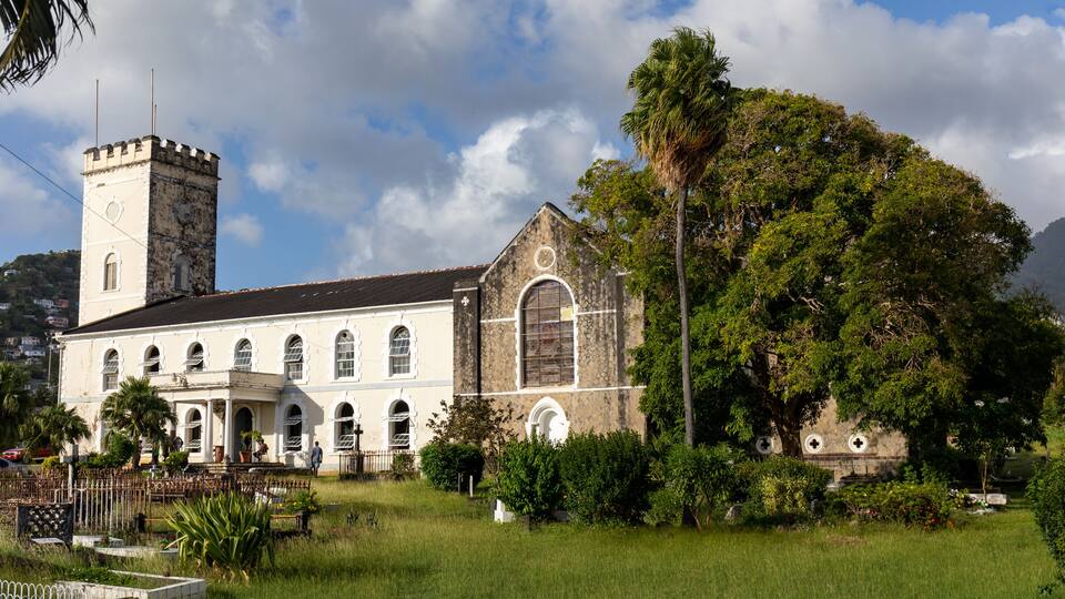 A historic church with a clock tower and a large tree in front.