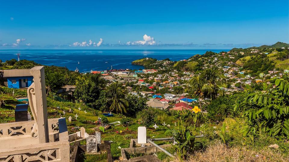 A coastal town with a view of the ocean, green hills, and colorful houses.
