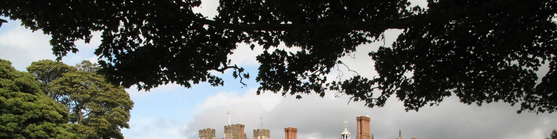 A large, historic stone building with multiple towers and turrets, surrounded by a grassy field and trees.