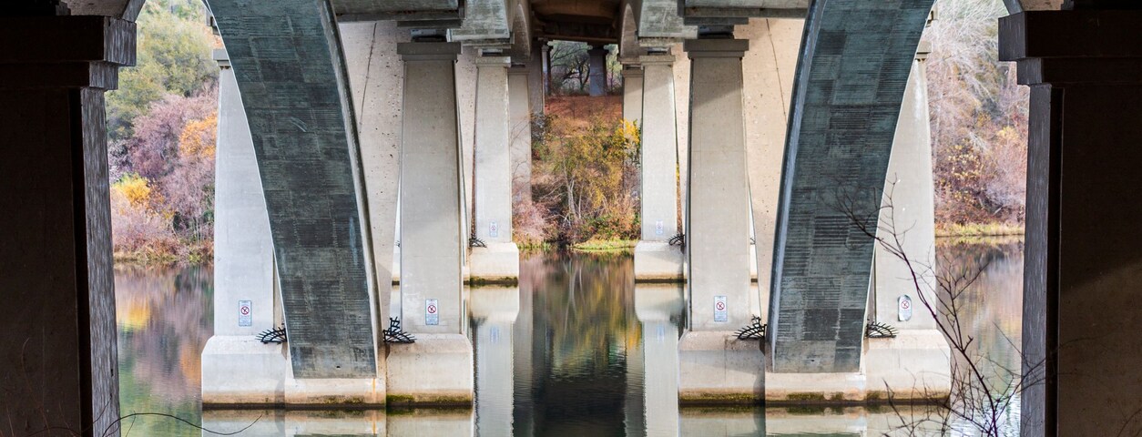 Un puente de piedra con arcos sobre un río tranquilo que refleja la estructura.