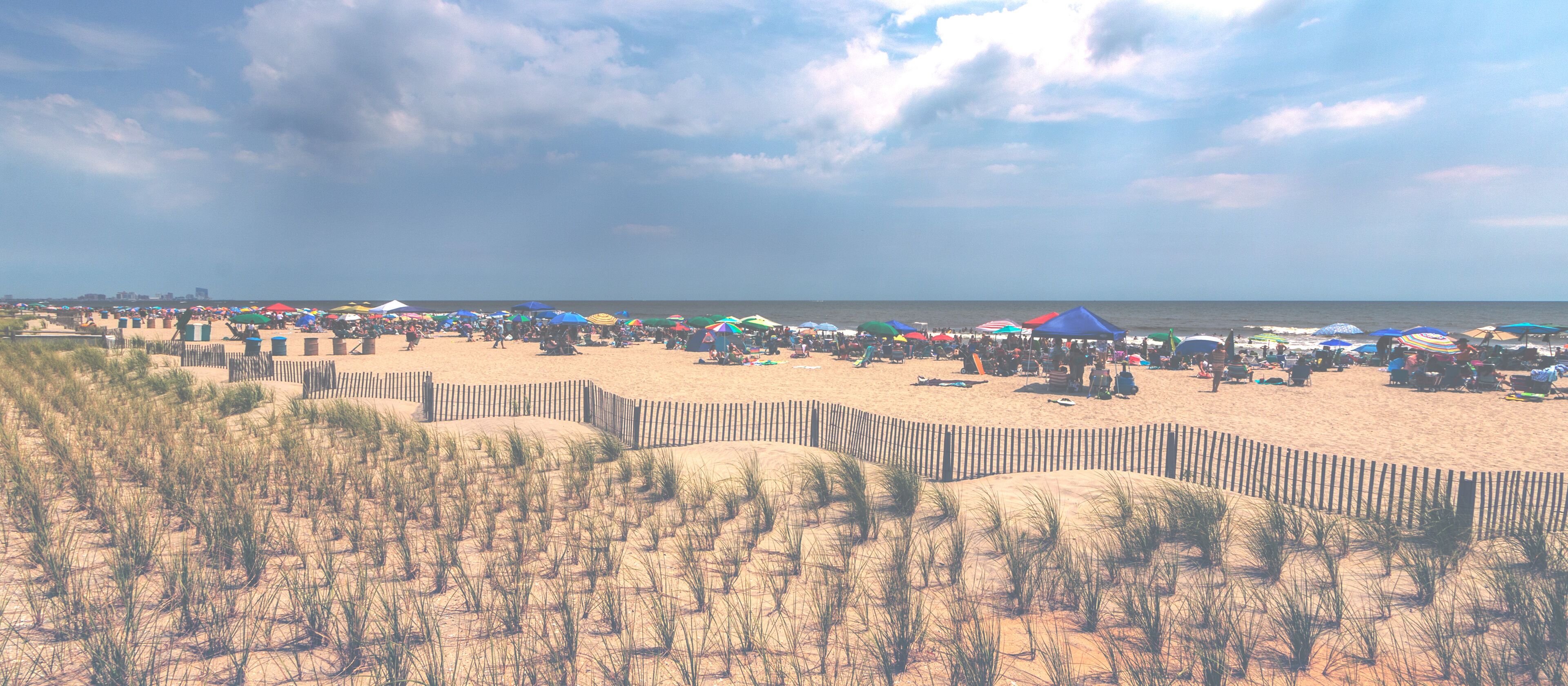 A beach with a wooden fence, people, and colorful umbrellas.