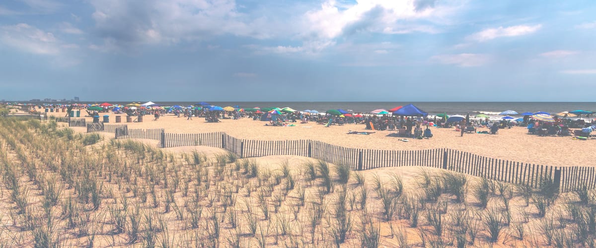 A beach with a wooden fence, people, and colorful umbrellas.