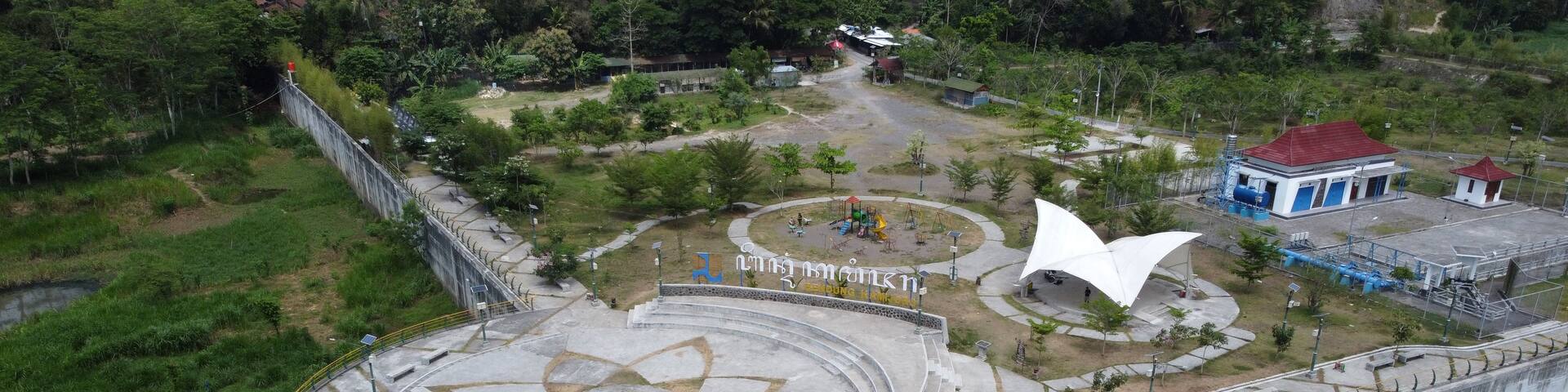 A large concrete dam with a circular plaza featuring a star-shaped design, surrounded by greenery and a small playground.