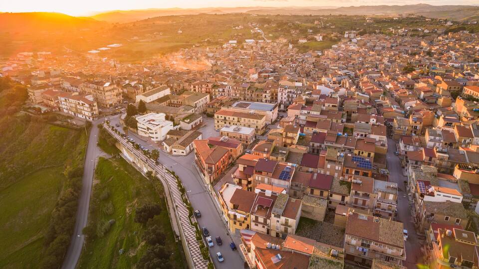 An aerial view of a densely packed town with a mix of traditional and modern buildings, surrounded by green hills.