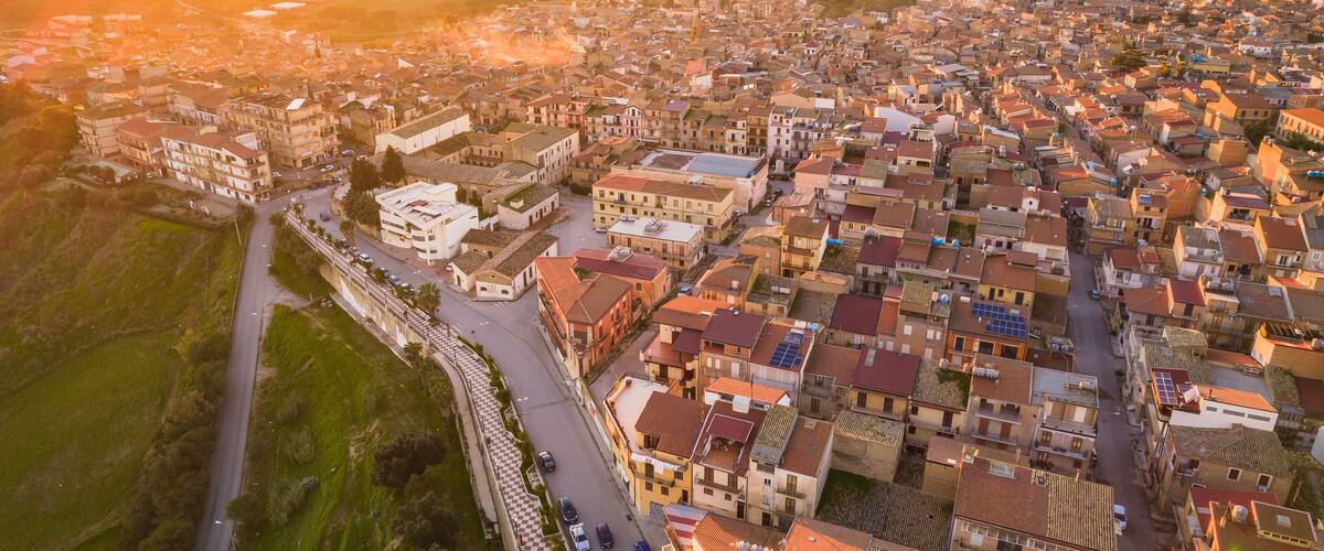 An aerial view of a densely packed town with a mix of traditional and modern buildings, surrounded by green hills.