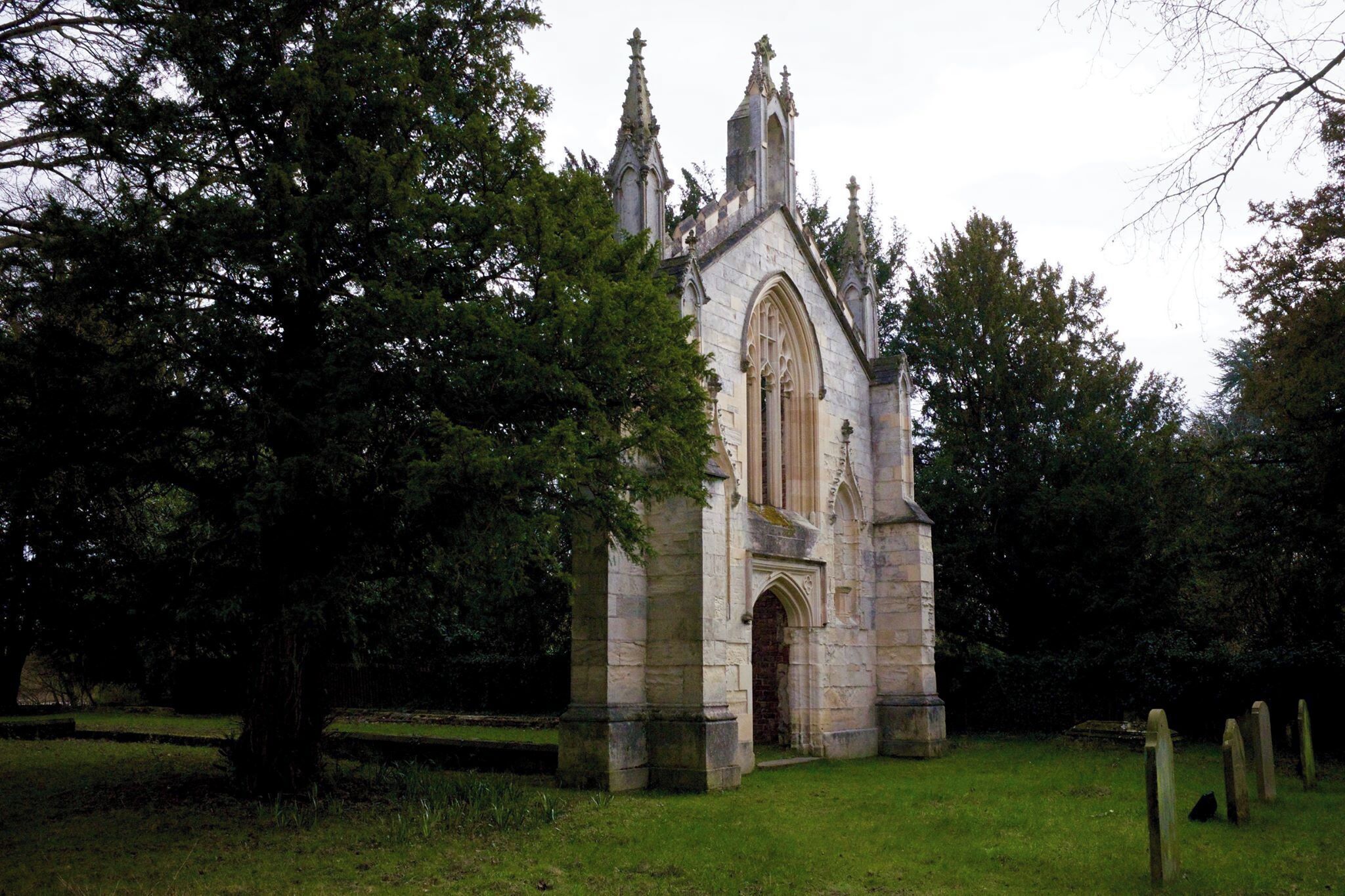 A historic stone church with a tall tower and pointed arches, surrounded by trees and a grassy area.