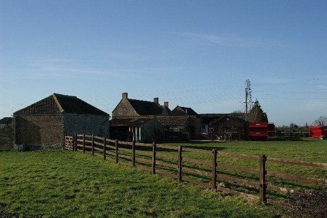 A rural farmstead with stone buildings, a wooden fence, and a red silo.