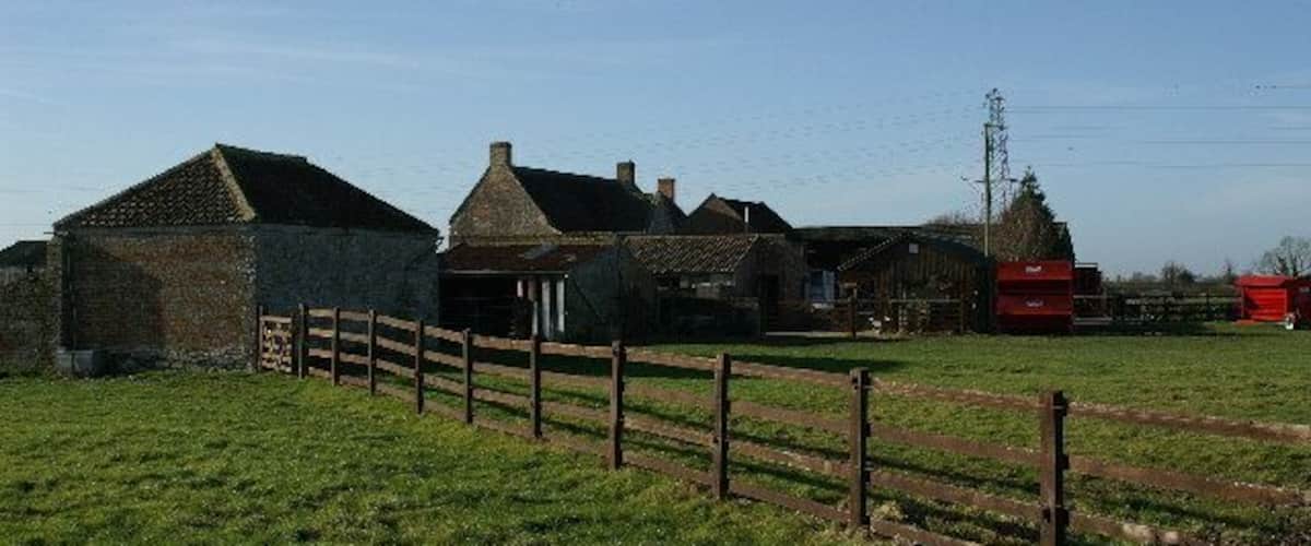 A rural farmstead with stone buildings, a wooden fence, and a red silo.