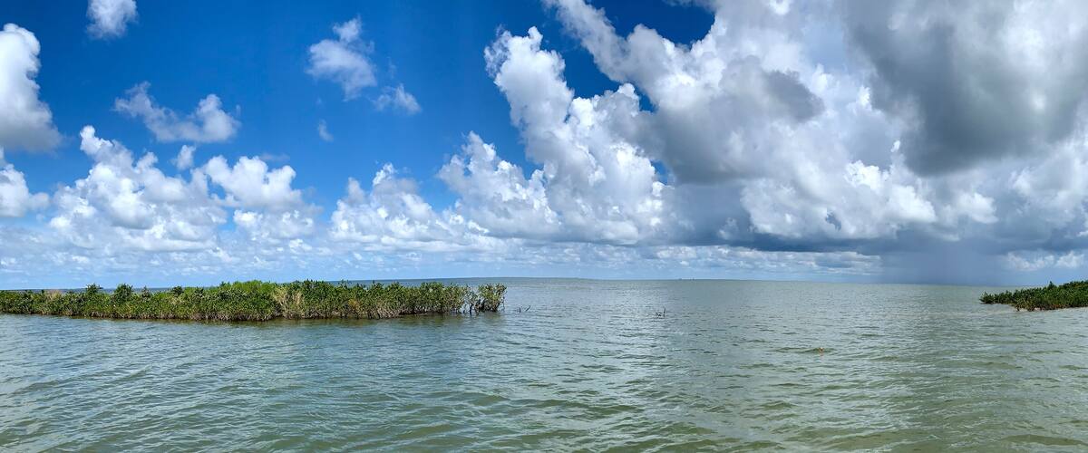 A calm sea with a clear sky and scattered clouds.