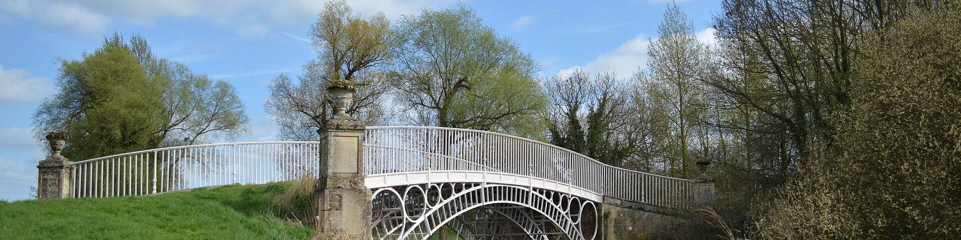A white stone bridge with a decorative arch over a grassy hill.