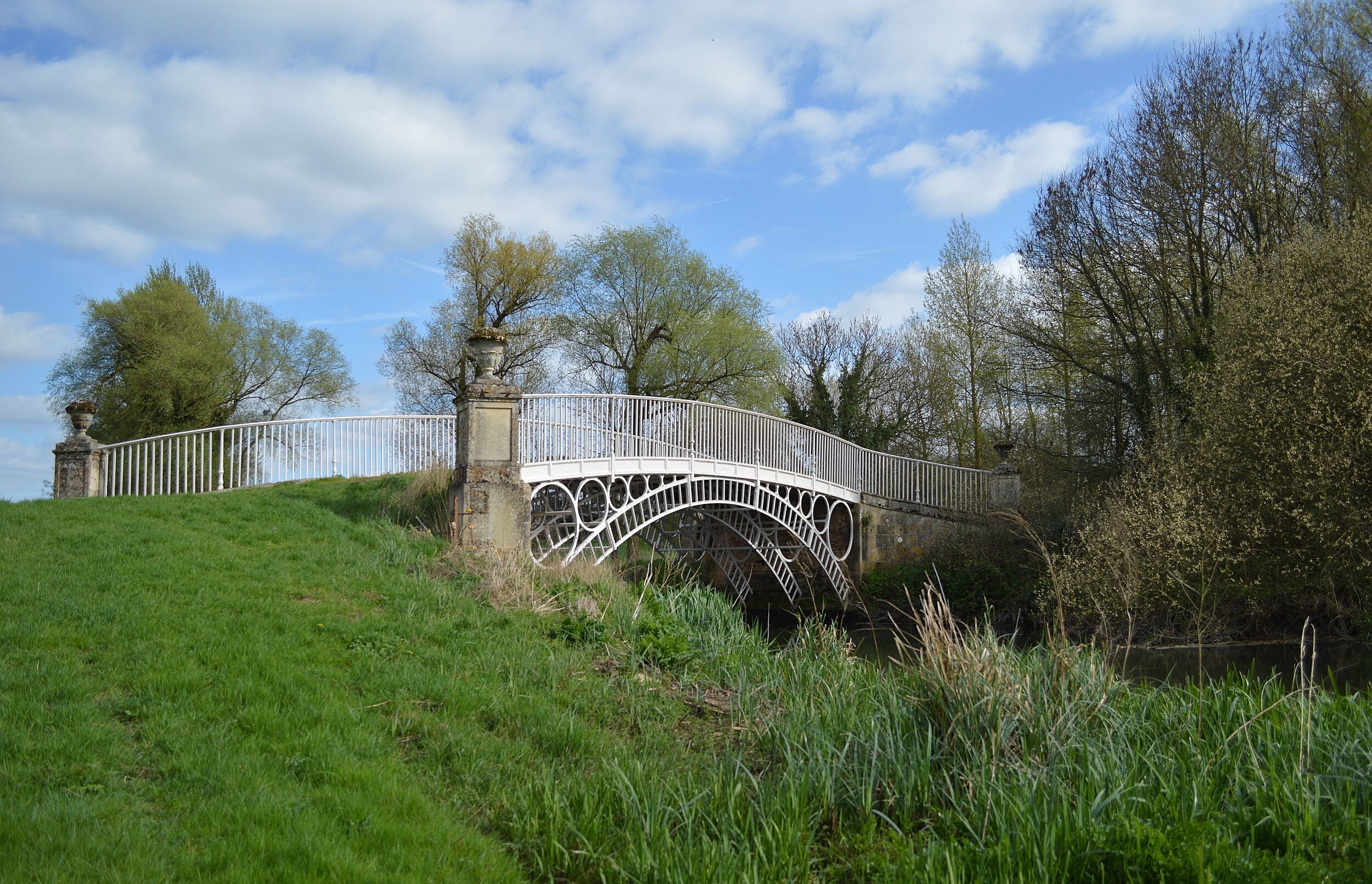 A white stone bridge with a decorative arch over a grassy hill.