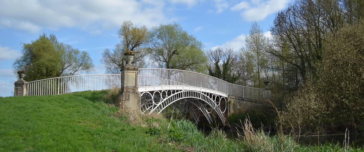 A white stone bridge with a decorative arch over a grassy hill.