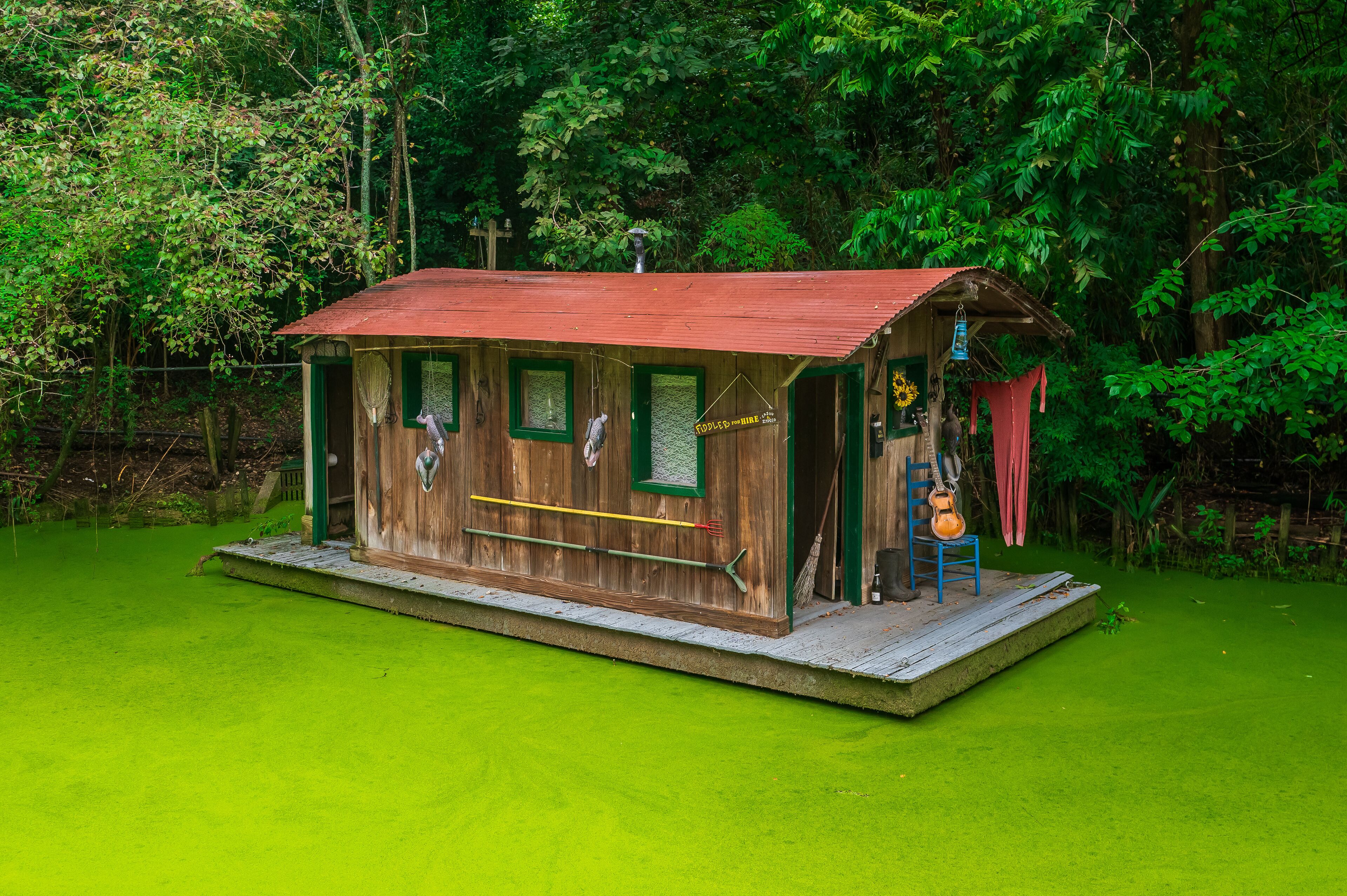 A rustic wooden cabin with a red roof, surrounded by lush greenery.