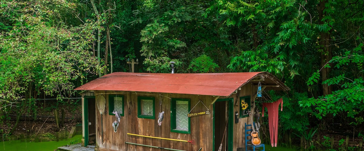 A rustic wooden cabin with a red roof, surrounded by lush greenery.
