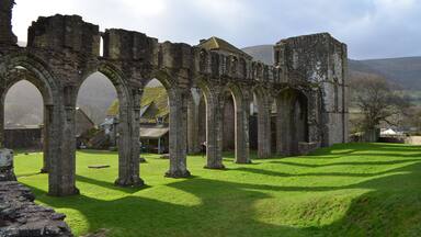 A historic stone structure with arches and ruins, surrounded by green grass and a clear sky.