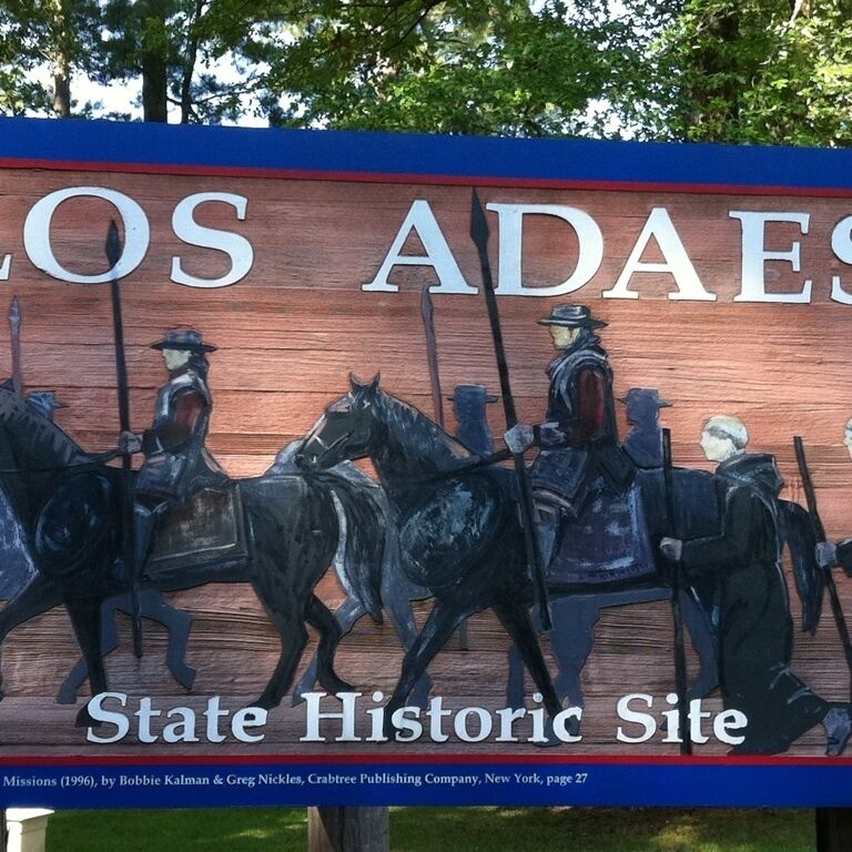 A wooden sign with 'LOS ADAES State Historic Site' and a depiction of soldiers on horseback.