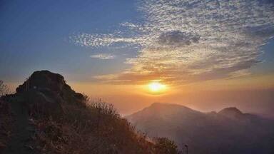 Un coucher de soleil sur un paysage montagneux, avec un sommet proéminent au premier plan.