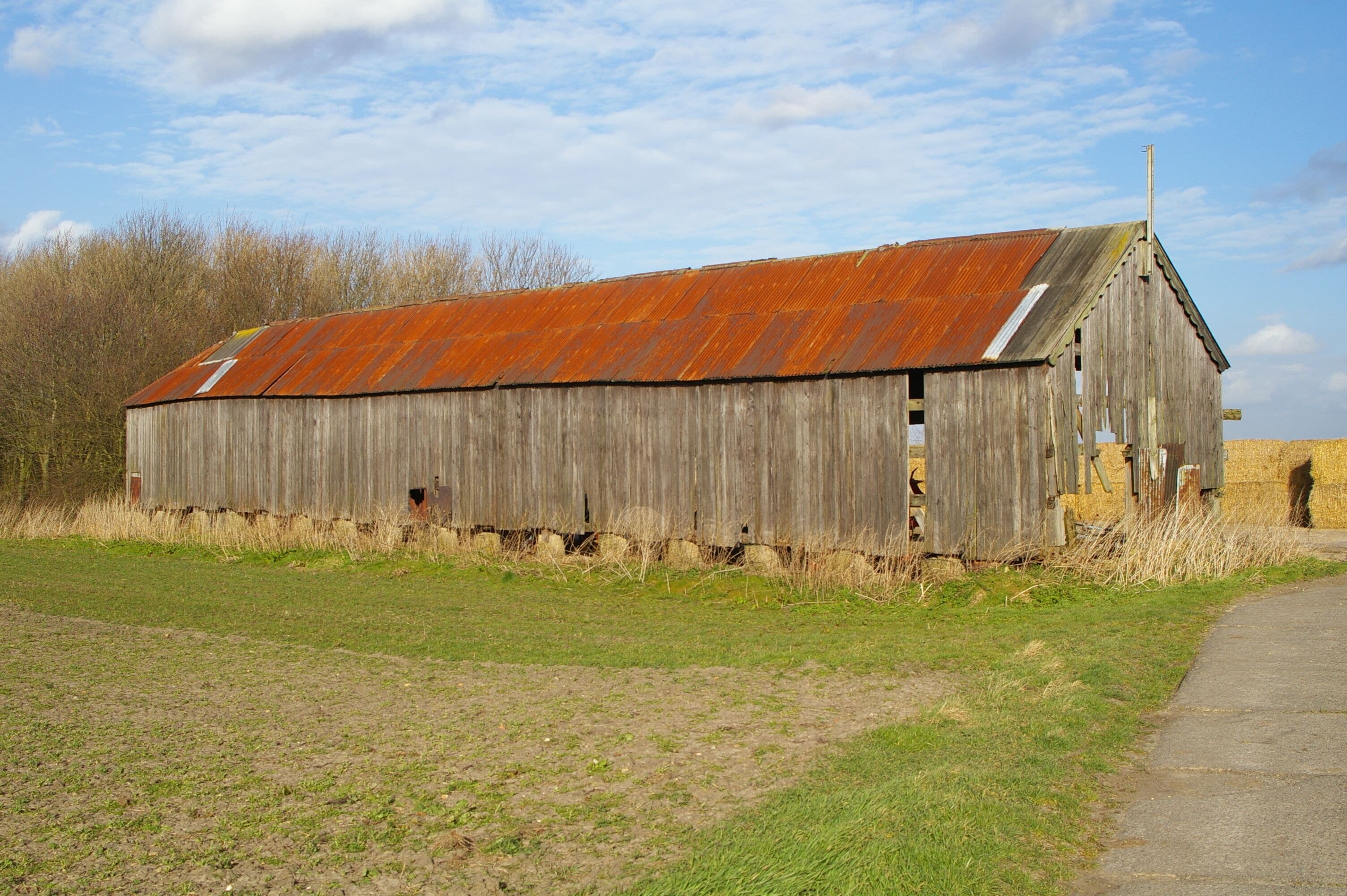 A weathered wooden barn with a rusted roof in a rural setting.