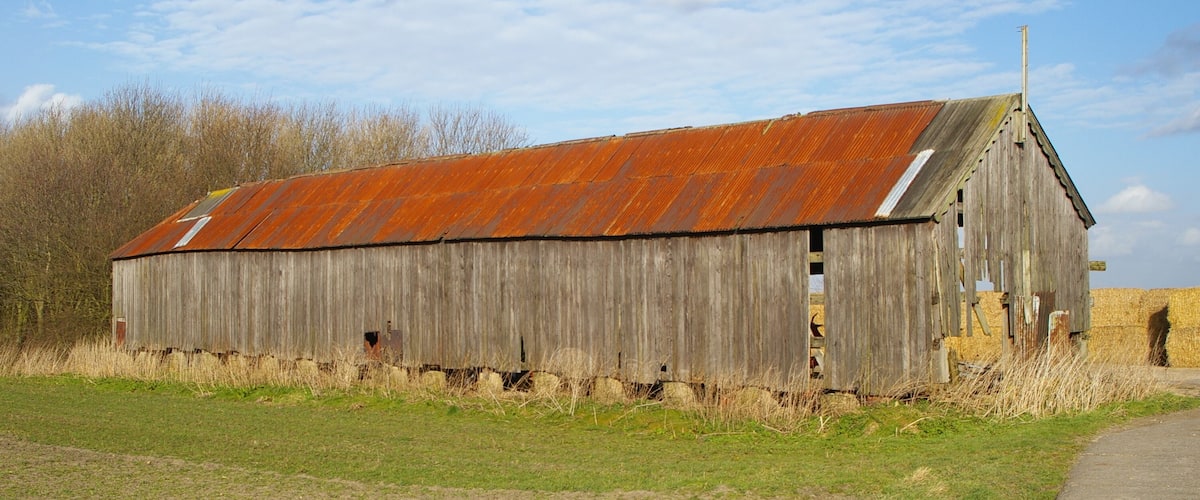 A weathered wooden barn with a rusted roof in a rural setting.