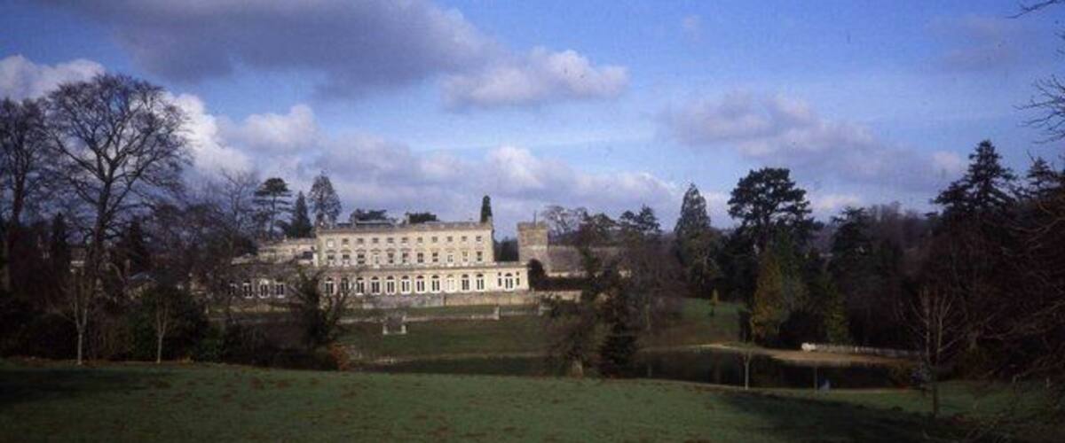 A large, historic building with a symmetrical facade, surrounded by a well-maintained lawn and trees.