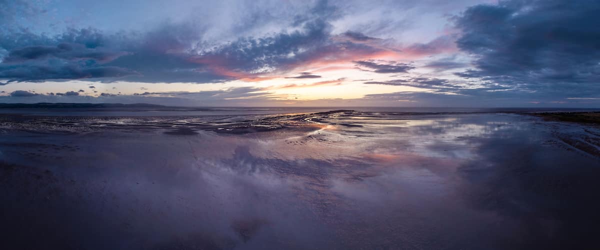 A sunset over a wet beach with a cloudy sky.