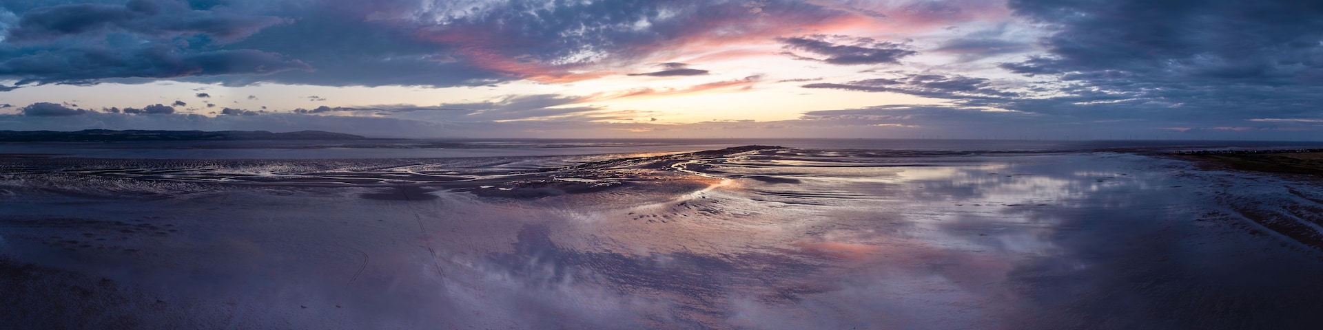 Un atardecer sobre una playa mojada con cielo nublado.