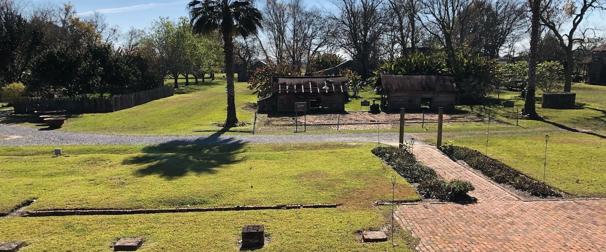 A well-maintained grassy area with a brick pathway, palm trees, and a rustic building.