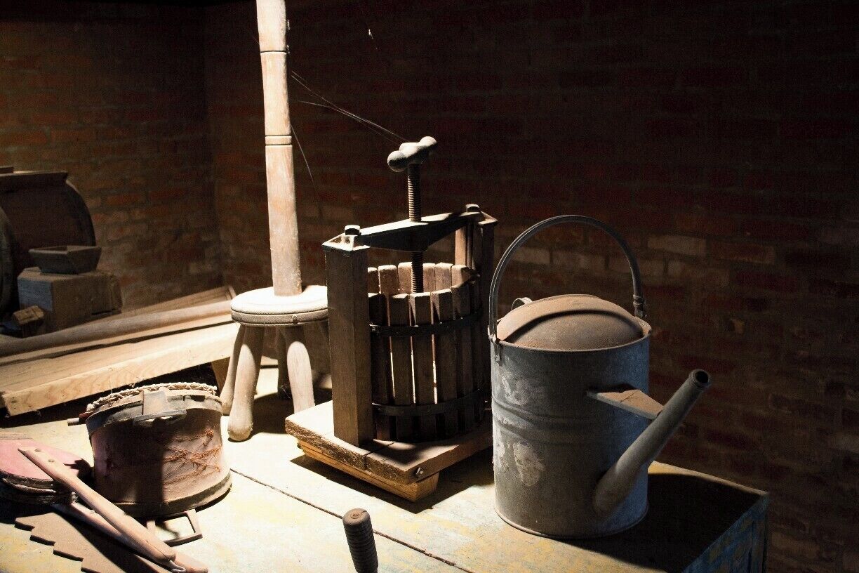 A rustic kitchen with a wooden stove, a metal pot, a wooden press, and a metal bucket.