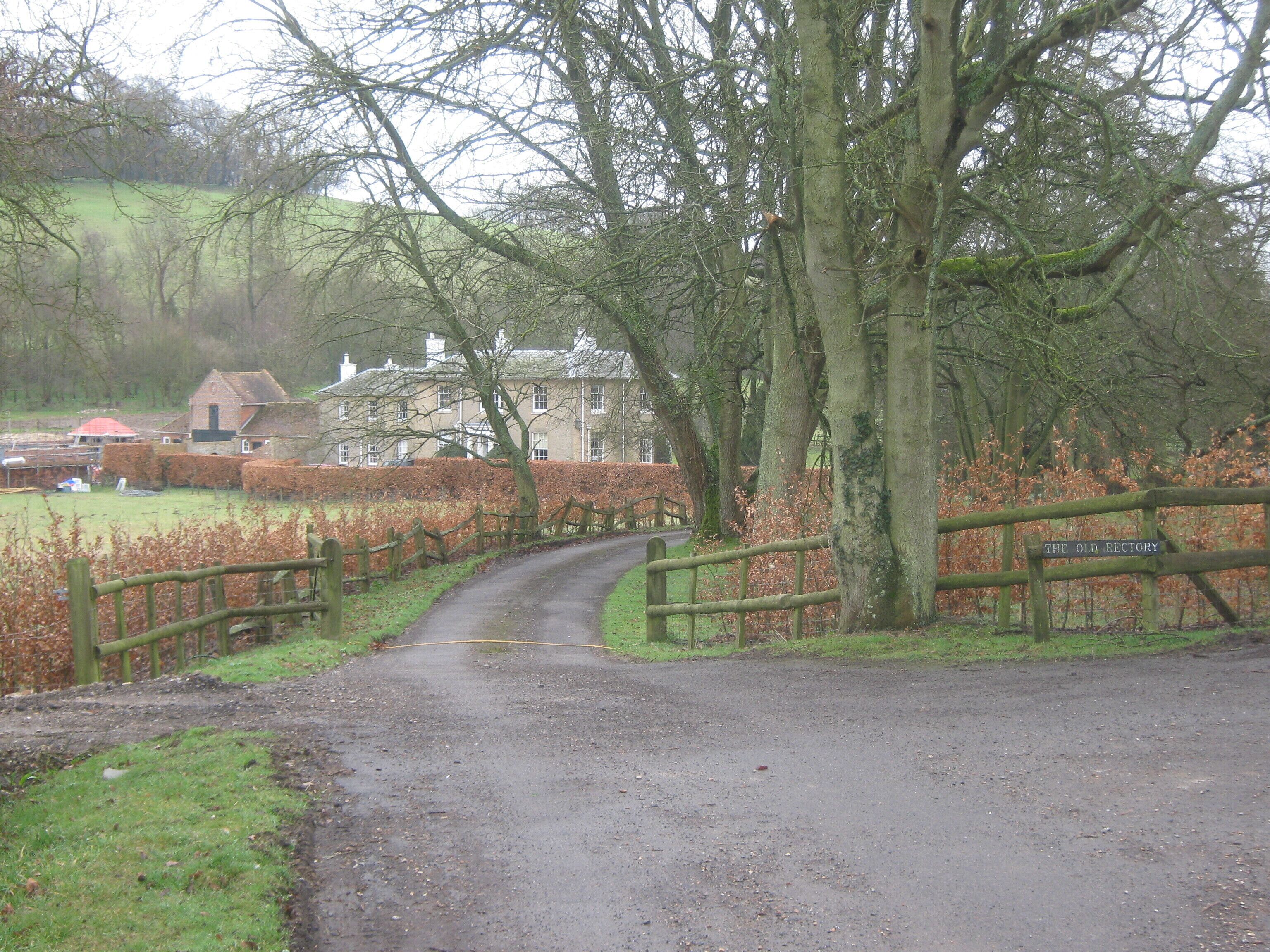 A rural road leading to a property named "The Old Rectory" surrounded by trees and a hedge.