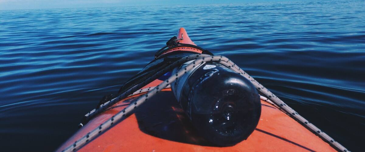 A boat's bow with a rope and a black object, likely a winch, on a calm sea under a clear blue sky.