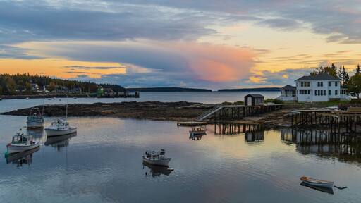 A coastal scene with boats, a dock, a white house, and a forested island in the background.