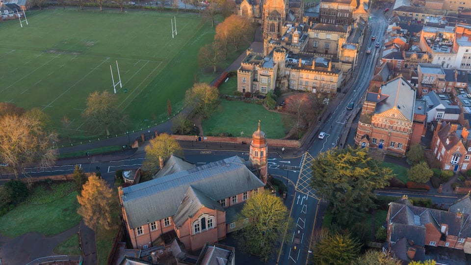 Aerial view of golden sunlight bathing Rugby School's historic buildings and grounds with the town sprawling beyond, a blend of old and new, Rugby, England, United Kingdom.