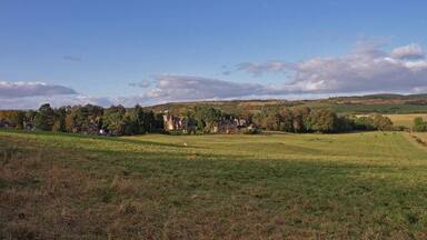 A rural landscape with rolling hills, a large field, and a historic building in the distance.