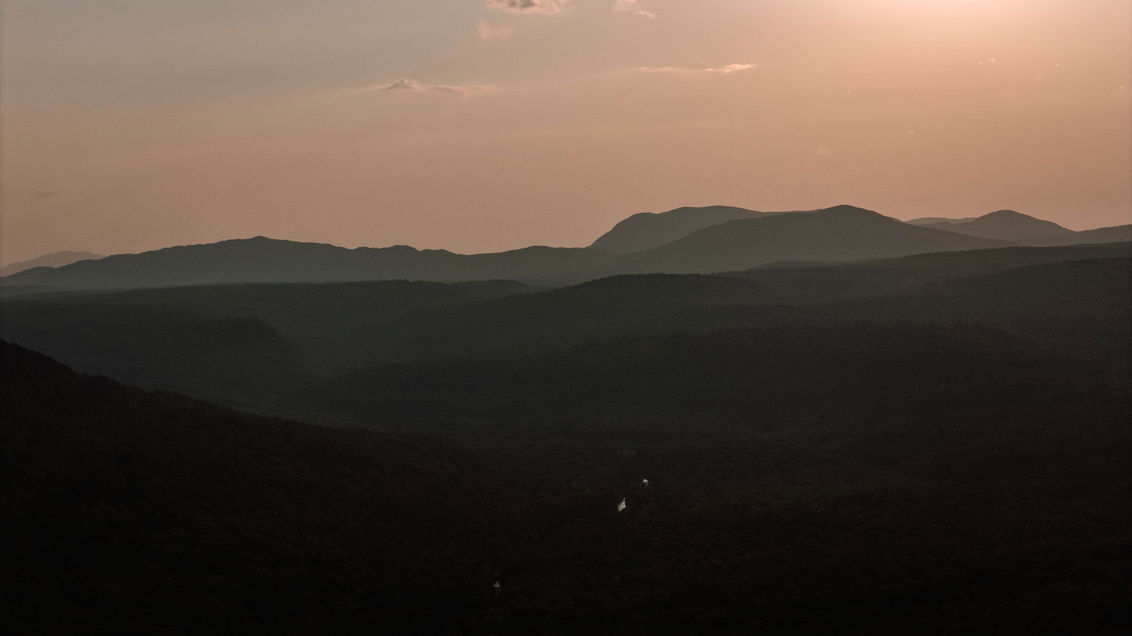 A mountain range with a valley in the foreground and a sun setting in the background.