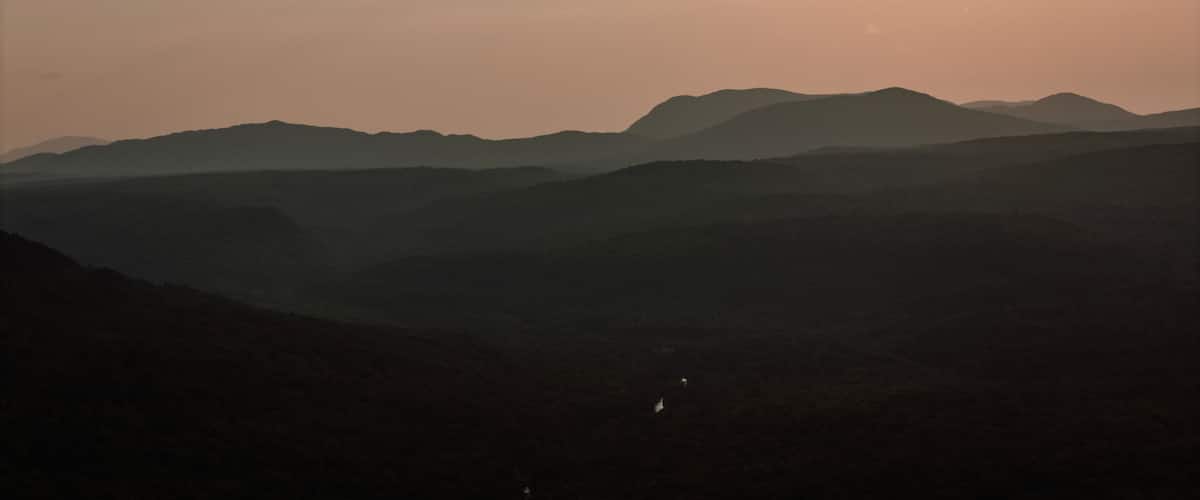 A mountain range with a valley in the foreground and a sun setting in the background.