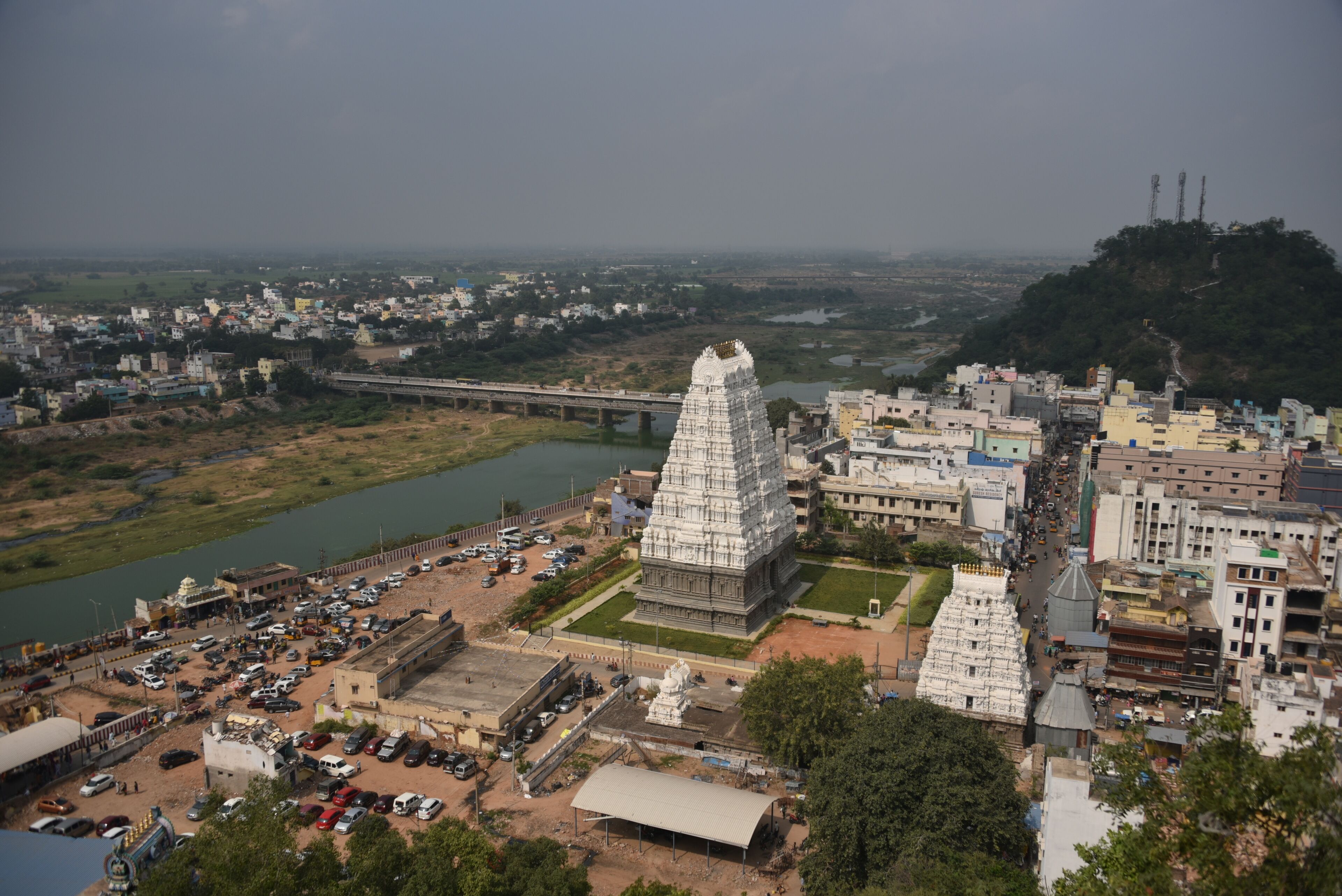 A temple complex with a large central tower, a river, and a bridge in the background.