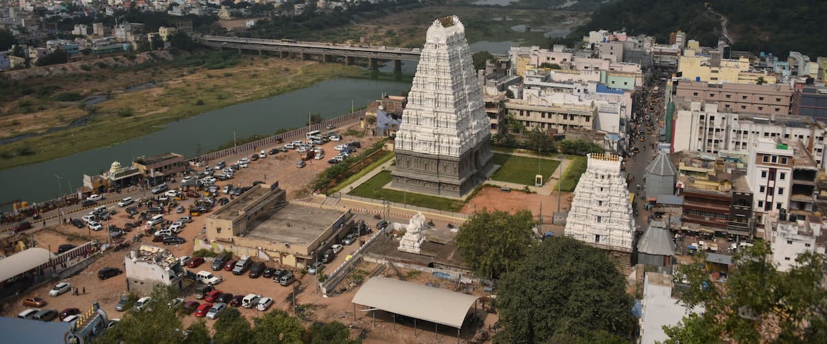 A temple complex with a large central tower, a river, and a bridge in the background.