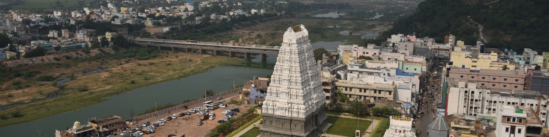 A temple complex with a large central tower, a river, and a bridge in the background.