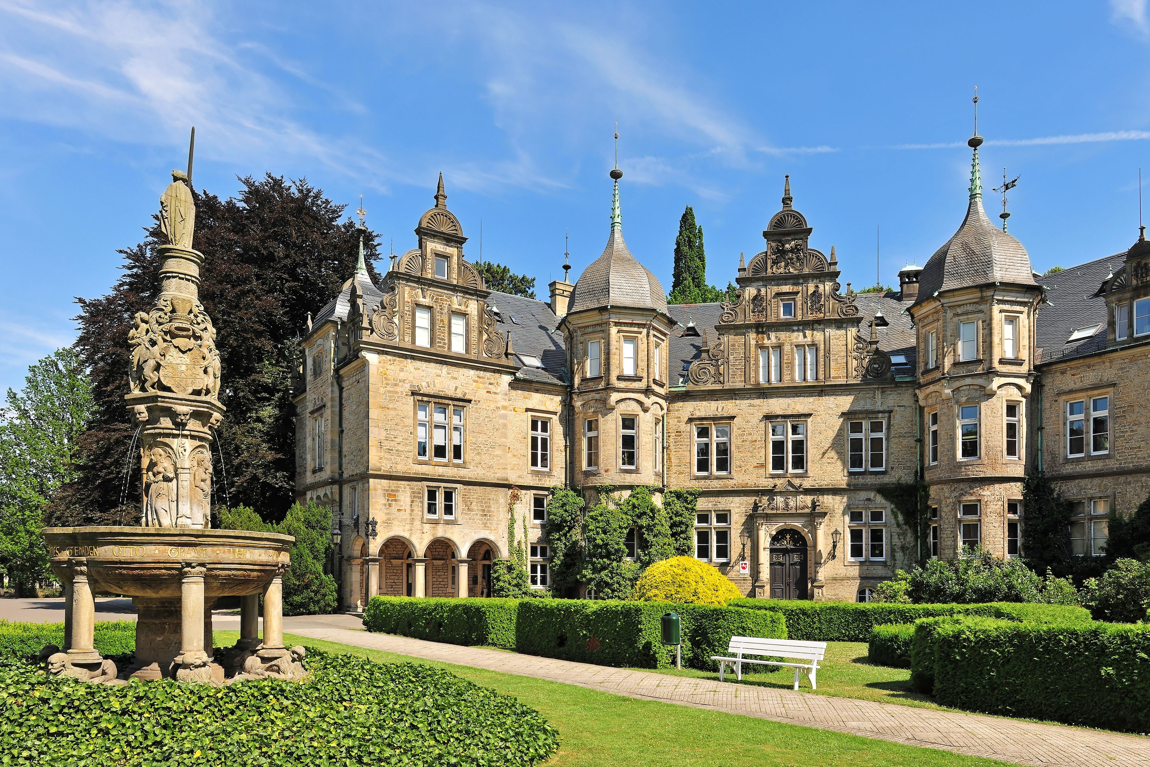 A historic building with ornate architecture, a fountain, and well-maintained gardens.