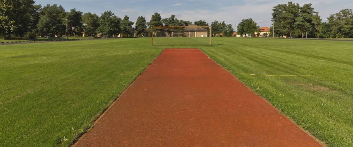 A sports field with a red track and goalpost, surrounded by trees and buildings.