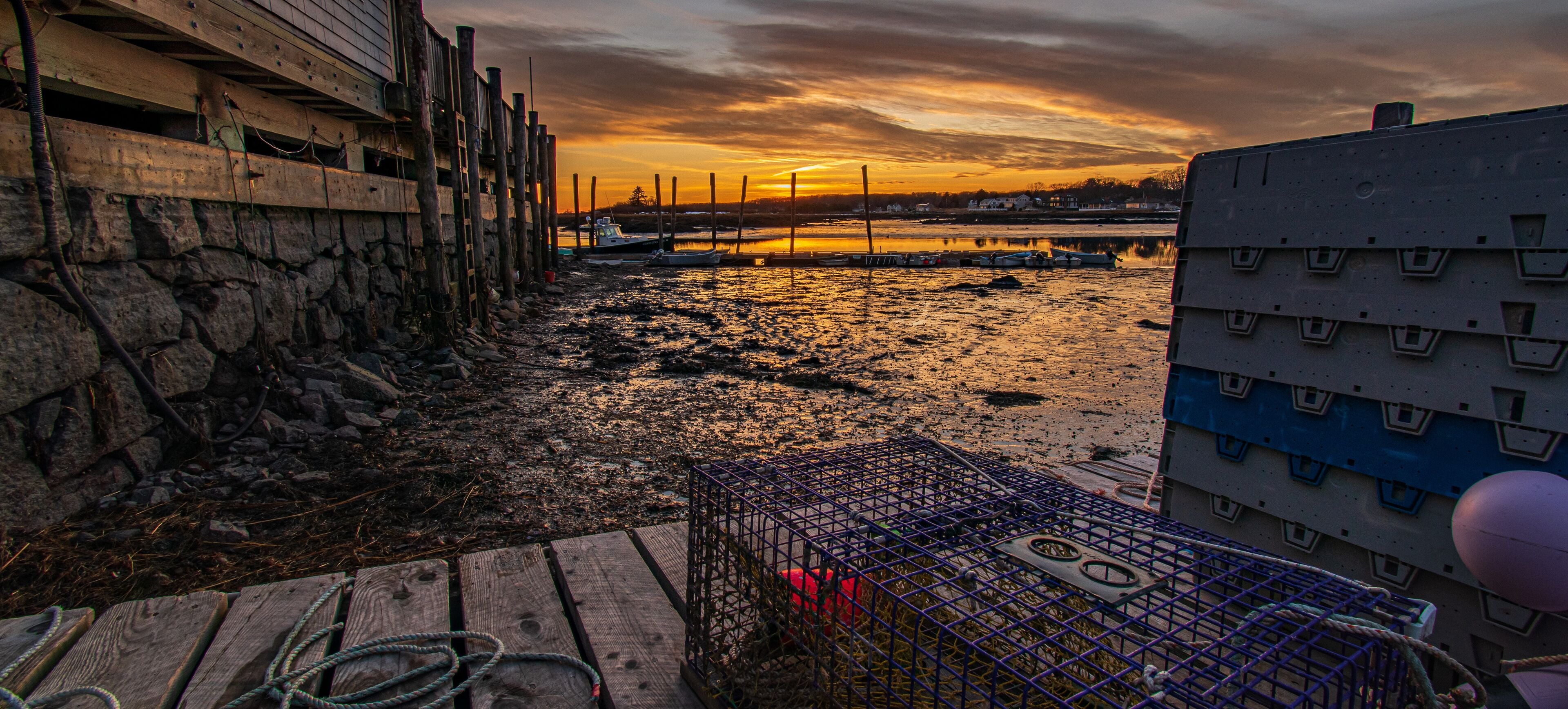 A sunset over a rocky shoreline with boats and a wooden pier.