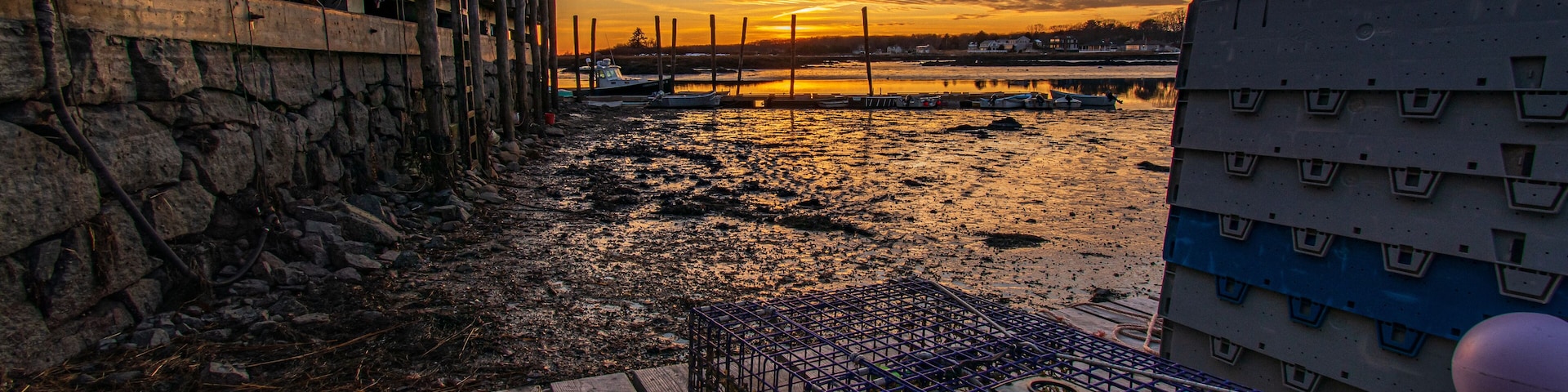 Um pôr do sol sobre uma costa rochosa com barcos e um cais de madeira.