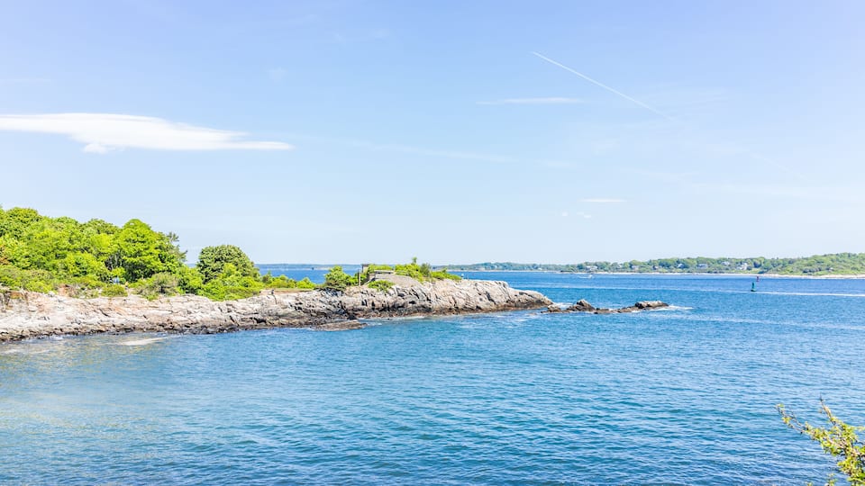 A coastal landscape with rocky shores, dense green foliage, and calm blue waters.