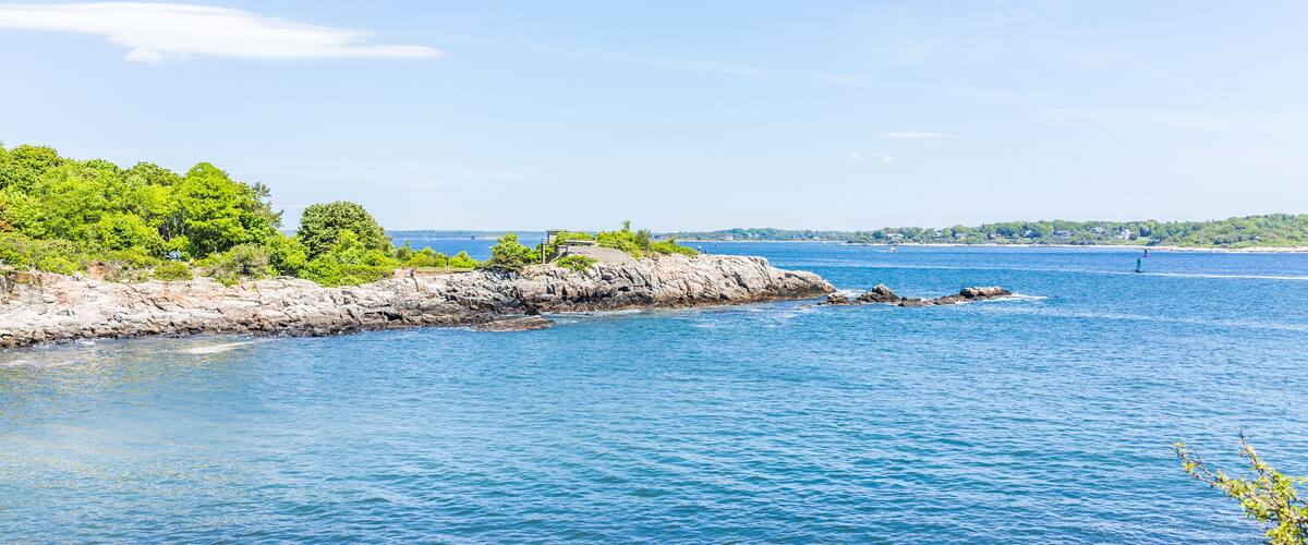 A coastal landscape with rocky shores, dense green foliage, and calm blue waters.