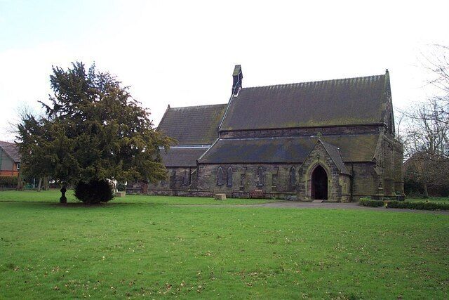 A church with a large tree in front, a stone building, and a clear sky.