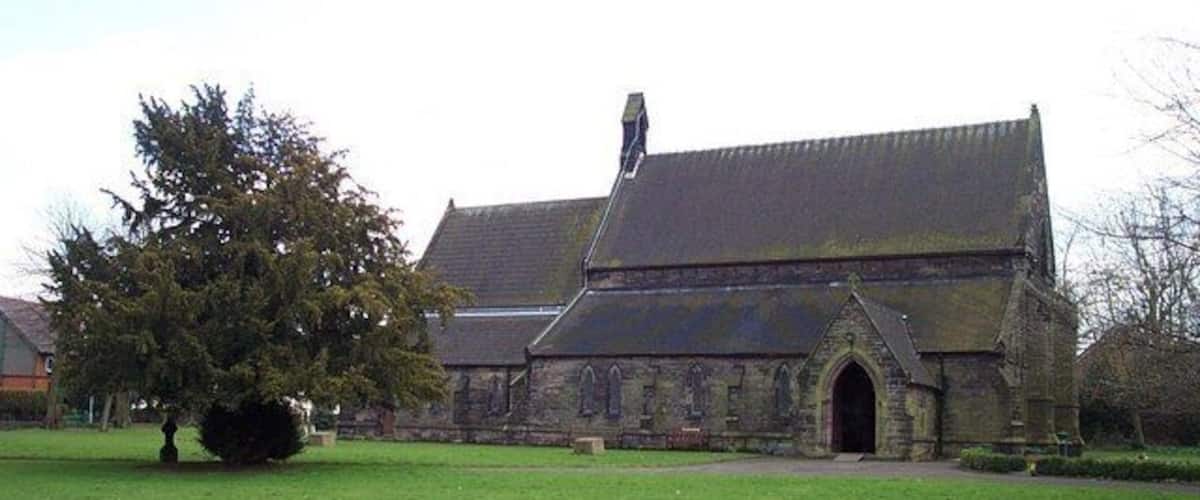 A church with a large tree in front, a stone building, and a clear sky.