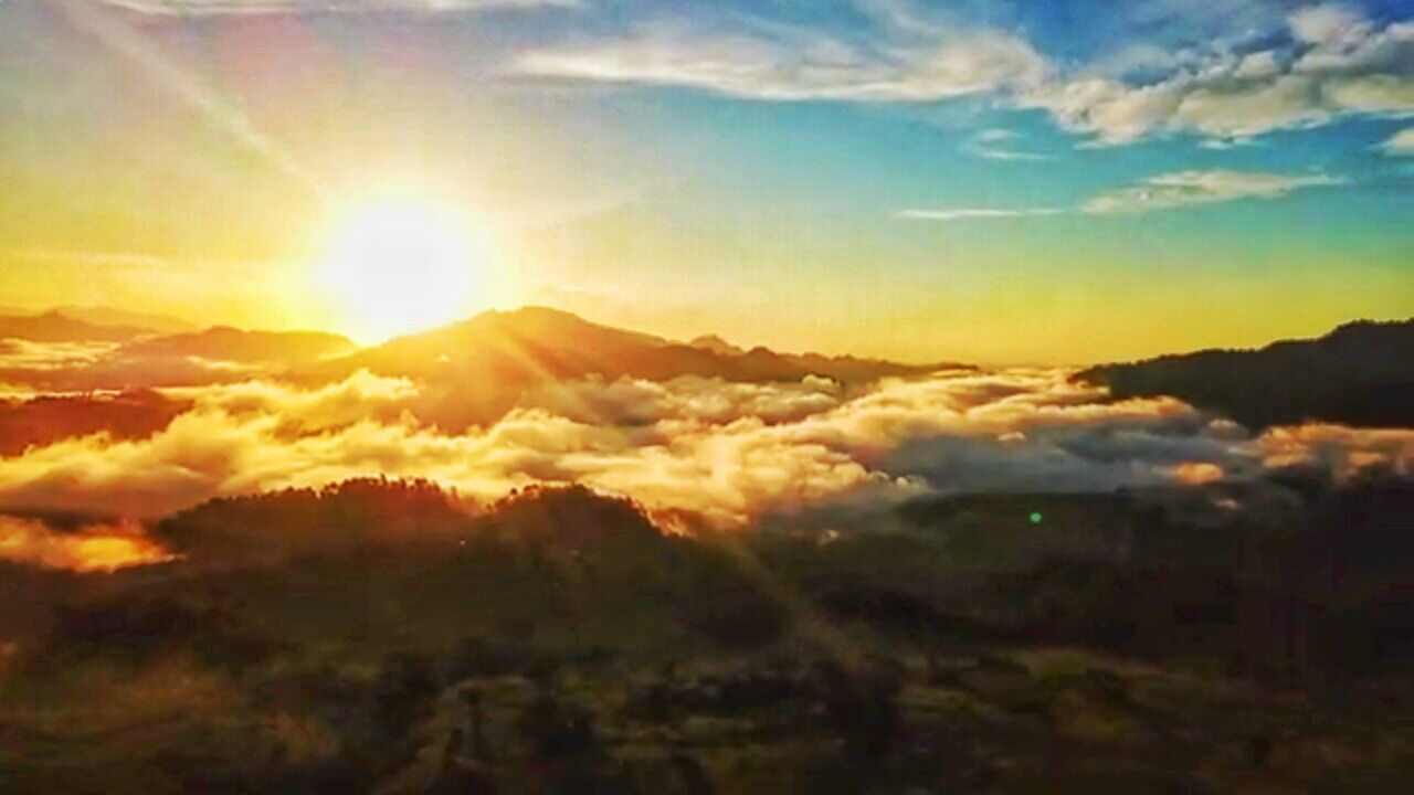A sunrise over a mountainous landscape with clouds below the peaks.
